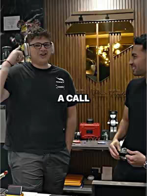 Two men in a well-lit room, one wearing glasses and headphones, pointing upwards, the other holding a smartwatch.