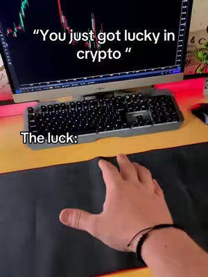 The image shows a person's hand over a black mousepad, with a computer setup in the background. The monitor displays a stock chart, a keyboard sits in front of it, and the text overlay reads "You just got lucky in crypto".