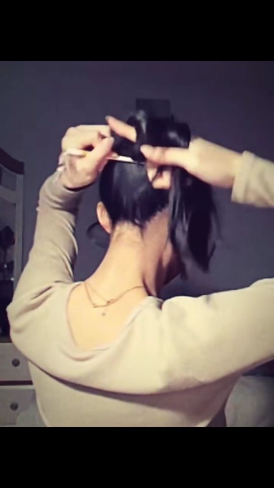 The cover image shows a woman from the back, with dark hair. She is in the process of styling her hair, holding it up with one hand and using a hair tool in the other. She wears a light-colored long-sleeved shirt. The background is out of focus, suggesting an indoor setting.
