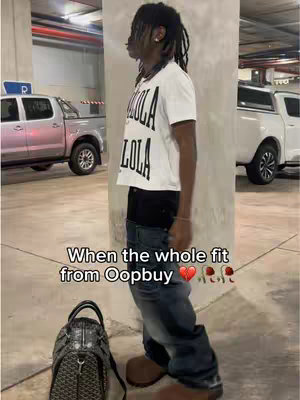 A person stands in a parking garage, wearing a white t-shirt with black print, jeans, and brown boots. A black backpack sits nearby. The image has overlaid text at the bottom.