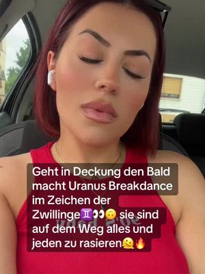 A woman with short red hair is looking towards the camera with slightly closed eyes. She's sitting in a car with sunglasses on her head and an earbud in one ear. There is overlaid text in a white box at the bottom of the image, and a red top.