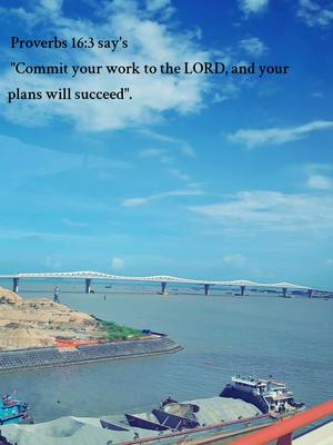 The image captures a scenic view with a bridge spanning across a wide river under a bright, blue sky dotted with fluffy clouds. In the foreground, a portion of a red barrier is visible, suggesting the perspective of someone overlooking the scene. The middle ground is dominated by a calm river, a bridge, and a landscape of water craft. Text is overlaid on the image, presenting a quote from Proverbs.