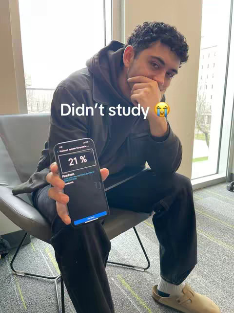 A young man is sitting in a chair, looking at his phone with a concerned expression. Text overlayed on the image reads "Didn't study" above his head. The background includes natural lighting from a large window.