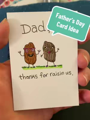 A close-up shot of a handmade Father's Day card held in a person's hand. The card is white and features a drawing of two anthropomorphic raisins, one wearing glasses and the other with lipstick. Above the raisins, it reads 'Dad'. Below the raisins are the words 'thanks for raisin us.' A speech bubble at the top right corner of the card says 'Father's day card idea.'