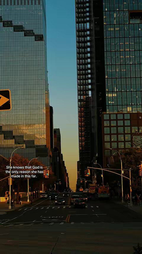 The image captures a vibrant cityscape with two tall buildings framing a street view. The buildings are glass-fronted, reflecting the sky and surrounding environment. The street below is filled with cars, and the perspective draws the eye towards the horizon where the sun is setting, casting warm hues. Text is overlaid on the upper left corner of the scene..