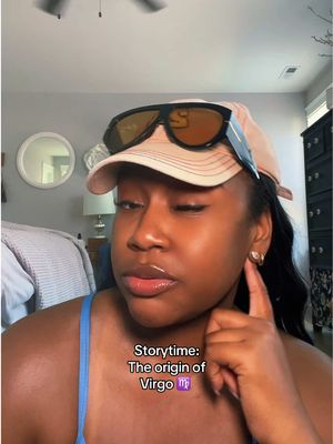 A woman with dark skin wearing a light pink baseball cap that partially obscures her dark hair. She is also wearing large black sunglasses on top of the hat. She wears earrings and a blue tank-top. Text overlays at the bottom in white. The background is a room with a grey wall and a mirror.