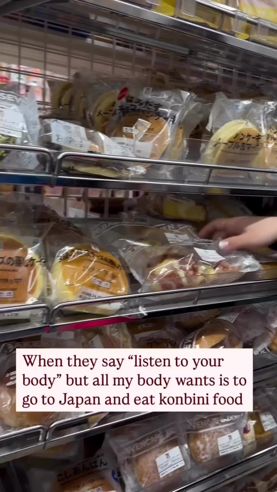 A well-lit shot inside a Japanese convenience store. The shelves are filled with individually wrapped food items, mostly bread and pastries. The camera angle is from a slightly low perspective, emphasizing the array of products. The background is slightly blurred, keeping the focus on the food items, and the hand is reaching for a product. A text overlay is at the bottom, reading. The overall composition is bright and inviting.