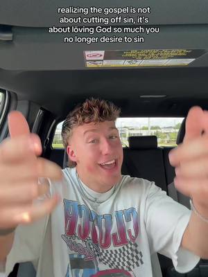 A man is seated inside a car, looking towards the camera with a slight smile and gesturing with both hands. The hands are open and towards the camera. Behind him, a car interior is partially visible, including the headliner and a headrest. Text overlay, positioned at the top, discusses the meaning of the Gospel.