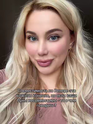 A close-up shot of a fair-skinned woman with long, wavy blonde hair. She has rosy cheeks, blue eyes, and pink lips. The background is blurred, and she is wearing a light-colored top with the beginning of the neck of a pink one visible. Text overlays the image, with the text displayed in white against a dark semi-transparent background.