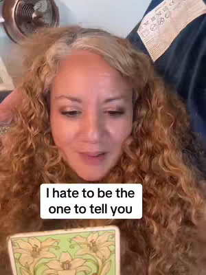 A woman with curly hair is holding a tarot card, a fan and a blue fabric are in the background. A white rectangle with black text that says
I hate to be the
one to tell you.
is overlaid on the image.