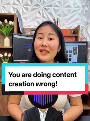 A woman with dark hair is centered in the frame, speaking and gesturing. Behind her is a white wall of geometric shapes, two computer monitors and various office supplies. A rectangular text overlay in light blue and white reads, 'You are doing content creation wrong!' A graphic of a person is visible with a suit.