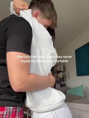 The cover image shows a close embrace between two people. The person on the left is wearing a black t-shirt and plaid pants. The other person is wearing a gray hoodie. The text overlayed on the image reads: "the fact that your touch has never made me feel uncomfortable". Behind the couple, there's a glimpse of a room with a bed, pillows and some shelves.