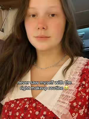 A young woman with long brown hair is featured, looking at the camera with a subtle expression. She wears a silver necklace and a white-collared, red floral dress. A text overlay states, 'never saw myself with the right makeup routine' with a smiling emoji.