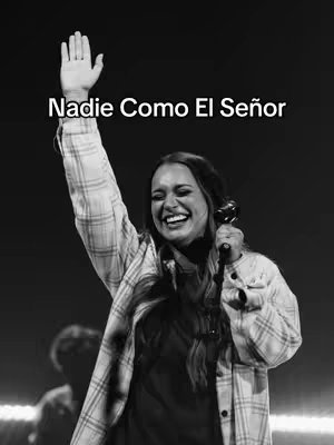 A black and white image features a woman with long hair, holding a microphone and smiling with one arm raised in the air. Text above her head reads, 'Nadie Como El Señor'. Her expression is joyful and the photo is well lit.