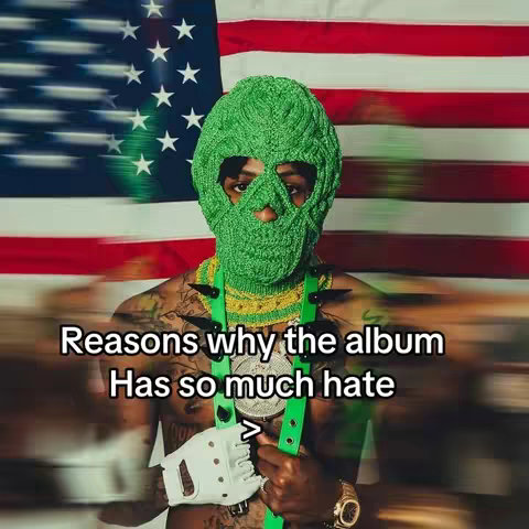 A person wearing a green knitted mask and holding a silver chain with spikes, is positioned in front of a blurry American flag. Text overlay reads 'Reasons why the album Has so much hate'.