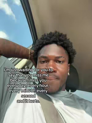 A close-up shot of a Black man in a car, gazing directly at the camera with a slightly concerned expression. He has short, dark, curly hair and is wearing a white and gray shirt. Text is overlaid on the image.
