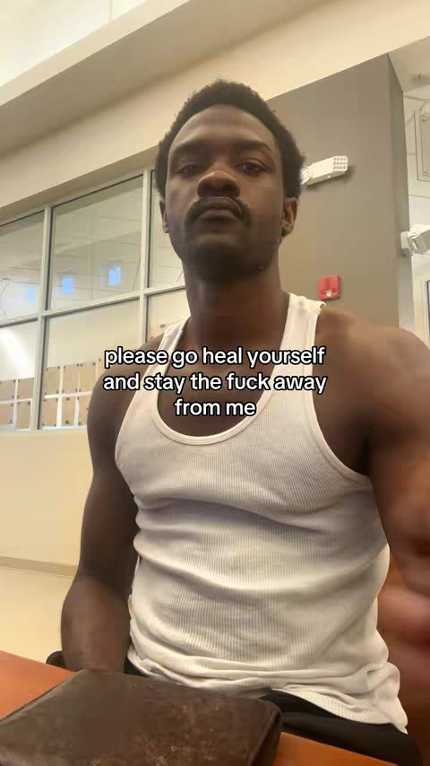 A man in a white tank top stands inside a building. He has short, dark hair and a serious expression. Text in a white font is overlaid on the image.