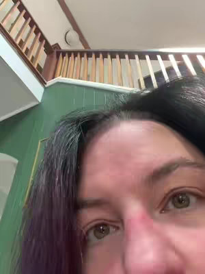 A close-up shot, angled towards the viewer's face and eyes. The upper portion of the image displays a wooden railing and a glimpse of a ceiling. The background features a green wall. The main focus is on a person's face, showcasing their eyes, eyebrows, and a portion of the forehead and nose. The lighting appears to be natural, casting subtle shadows.
