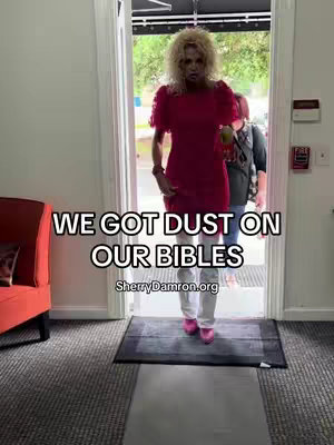 A woman in a red dress is standing in a doorway, with text overlayed on the image. Behind her, two other people are visible, partially obscured. The setting appears to be indoors with a neutral wall color and a glimpse of the outside through the door.