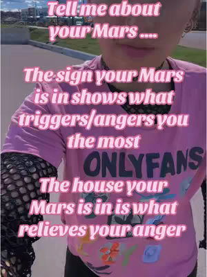 A selfie-style shot featuring a person wearing a pink shirt with text, set against a blurred outdoor backdrop. The individual's face is partially visible, with overlaid text in a stylized font addressing astrological themes related to "Mars."