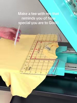 A person's hand using a pen to adjust a yellow t-shirt on a work station. A ruler lays over the shirt. Text is written on the upper half of the image.