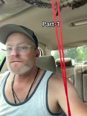 A man wearing glasses and a baseball cap is sitting in the front seat of a car. The front passenger seat is vacant. There is a red rope or wire in the frame.
