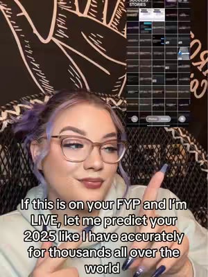 A woman with purple-tinted hair and glasses is seated, pointing towards the viewer. A display of app content is visible behind her.
