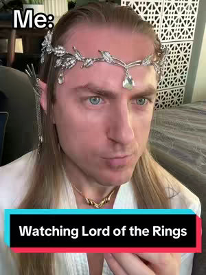 A selfie-style image shows a person with long, light-colored hair and a delicate silver crown with leaf and gem details. The person, wearing a white shirt and a gold necklace, has fair skin, and blue eyes. The background is blurred but appears to have a patterned surface. A colored bar at the bottom reads "Watching Lord of the Rings". Above the head, the text "Me:" appears.