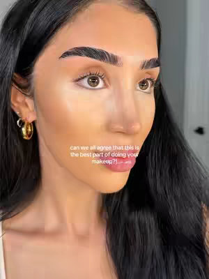 A close-up shot of a woman's face, focusing on her eyes and makeup. She has dark hair, thick eyebrows, and is wearing hoop earrings. Text overlies the image, asking if others agree that a certain step in makeup application is the best part.