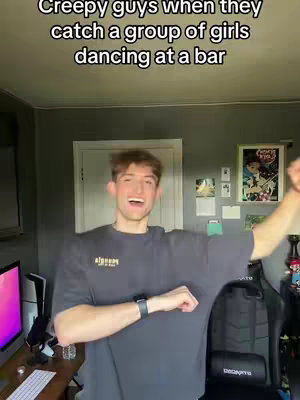 A young man with short brown hair is enthusiastically acting, his mouth open in a wide smile and his arms raised. Above him, text reads, 'Creepy guys when they catch a group of girls dancing at a bar.' The background includes a gray wall, a closed white door, and various decorative items.