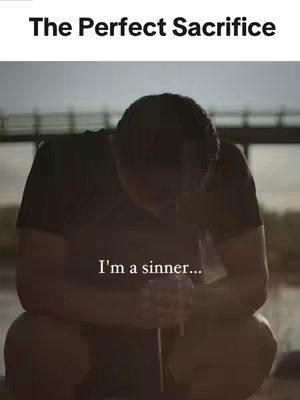 The image shows a person kneeling and bowed over, seemingly in a moment of reflection or prayer. Above them, text reads 'The Perfect Sacrifice'. The background is out of focus, with a bridge structure visible, giving the image a contemplative and possibly somber mood.