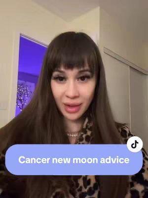 A woman with long brown hair and bangs is looking at the camera. She's wearing a patterned top with a necklace. A light blue oval banner reads, "Cancer new moon advice."