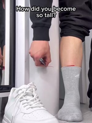 The image features a person's legs and a shoe by a wall with gray marker. The main focus is on a gray sock, and the person marks a line with the marker. The shoe, a sneaker, and the wall's stark white provide high contrast.