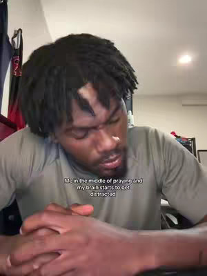 A man with dreadlocks looks down with a serious expression, hands clasped in front of him, likely praying or deep in thought. Text overlayed on the image provides further context to the scene.