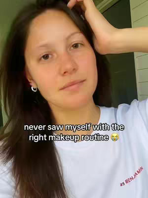A selfie-style image features a woman with dark hair and a white t-shirt, looking towards the camera. Text overlay reads, 'never saw myself with the right makeup routine.' The background is slightly blurred, suggesting an outdoor setting.