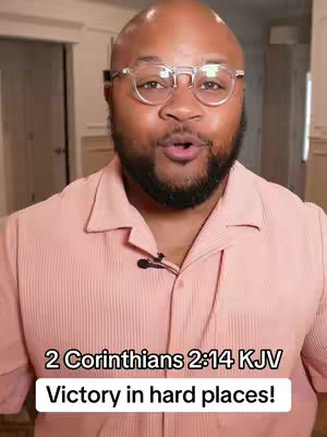 A medium shot of a Black man wearing glasses, a pink shirt, and a microphone. Below him is a text overlay with Bible verse details.