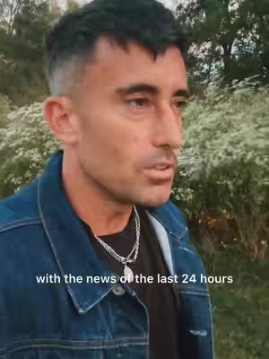 A man with short, dark hair and a denim jacket poses outdoors. The background is blurred, showing a mix of green foliage and trees. The text overlayed at the bottom of the image states: 'with the news of the last 24 hours'.
