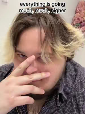 A selfie of a man partially covering his face with his fingers, looking at the camera. The text overlay reads "everything is going much, much, higher". The man has short brown hair with blonde highlights.