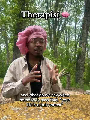 A person wearing a pink head covering and glasses, gesturing with their hands in front of a blurred outdoor background. Text overlays the image.