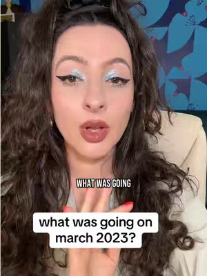 A woman with long wavy dark hair and sparkling silver eye makeup looks directly at the camera with a surprised expression. Text overlays in white boxes ask questions about what happened in March 2023. The background is a blurred blue with a floral pattern.