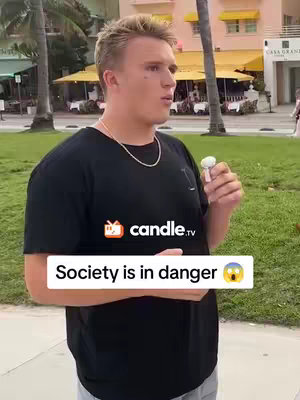 A young man with blond hair stands in a park-like setting with buildings in the background. He's wearing a black t-shirt and holding a wireless earbud. A text overlay states 'Society is in danger' with a surprised face emoji.