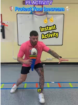 A man in a pink shirt and black shorts is in a gym. He is in a defensive stance, holding a blue ice cream cone prop in his hands, with the gym in the background. There are blue and orange lines on the floor to the creator's front.
