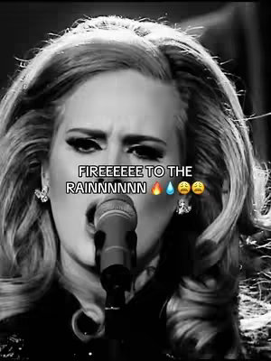 A black and white image featuring Adele performing on stage, with a microphone in front of her mouth. Overlaid text in white reads "FIREEEEE TO THE RAINNNNNN" with fire, water drop, and crying face emojis. The image is a close-up of her face, focusing on her expression as she sings.