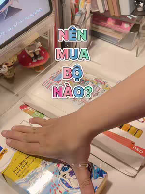 The cover image shows a hand reaching out towards various stationery items, with the question 'NÊN MUA BỘ NÀO?' overlaid. The hand is in the foreground, with colorful text bubbles, positioned over a table with several neatly arranged items which are stationery items.