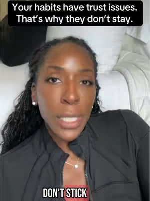 A woman with dark skin and braids is centered in the frame, gazing directly at the viewer. She appears to be in a bedroom, with white pillows and a bed visible in the background. Text overlays are present, with the most prominent one reading "DON'T STICK" in a bold, white font at the bottom of the screen. The woman is wearing a black top and has a necklace. The lighting is soft, and the overall composition suggests a personal or motivational video.