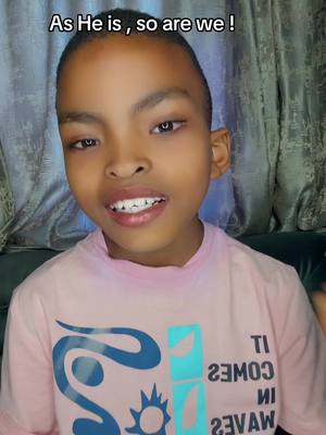 A young boy with short hair is the central focus. He is looking at the camera with a slight smile. The background is blurred, featuring curtains.