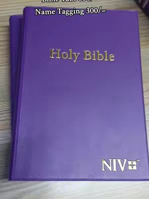 The image shows a closed purple Bible, with gold lettering of "Holy Bible" on the front. Below the "Holy Bible" text is "NIV" with gold lettering, the text "Bible Tabs 300/= and Name Tagging 300/= placed at the very top of the image.