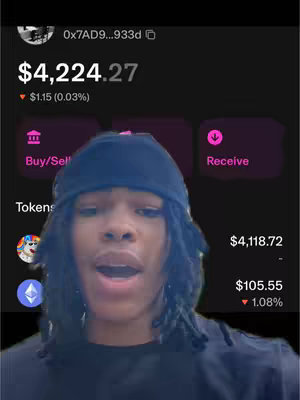 A selfie-style shot featuring a young man with a black beanie and dreadlocks, positioned in front of a digital display showing cryptocurrency transaction data. The screen has a dark background with light purple and white text for currency and values, and the man is centered, looking towards the camera with an open mouth. The overall lighting is neutral, bringing forward the display and the man’s face.