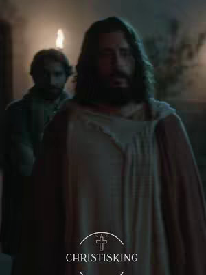 The image shows a scene from a religious film, likely depicting a moment from the Bible. A man with long dark hair and a beard, presumably Jesus, is in the foreground, dressed in white and brown robes. Beside him, slightly blurred, stands another figure. The background suggests a nighttime or indoor scene. The bottom portion is the text, placed within a graphic of a cross.