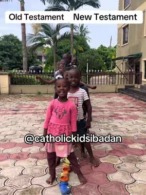 The cover image depicts a group of children standing in a line in front of a building. The central figure is a young girl in a pink top with a flower design, standing on toys. Behind her are other children. Above are vertical text labels "Old Testament New Testament". Overlaid is the text "@catholickidsibadan". The background includes trees and the side of a building with windows.